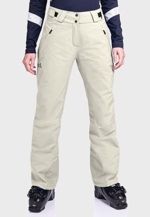 Schneehosen in Hellbeige, mit glatter Textur, verstellbarem Bund, Seitentaschen und verstärkten Bündchen. Getragen mit schwarzen Skischuhen.