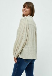 Blusa testurizzata beige chiaro con maniche lunghe a palloncino, scollatura rotonda e polsini con bottoni. Abbinata a jeans blu scuro.