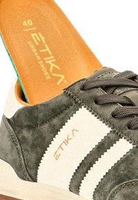 Zapatilla de ante verde y blanca con cordones marrones y una plantilla color beige etiquetada "ETIKA Urban Shoes" talla 40.