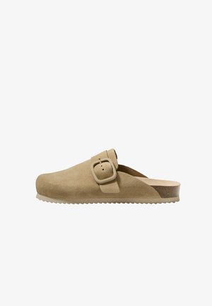 Beige ruskindstræsko med en rektangulær spænde og en tekstureret gummivoresole. Har en kork indersål og et rundt tådesign.