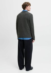 Pull en maille gris foncé à col rond, tissu texturé, porté par-dessus une chemise en denim bleu clair, associé à un pantalon noir ample.