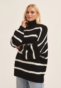 Black and white striped knit sweater with a high collar and oversized sleeves, featuring a textured fabric and loose fit.