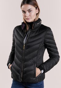 Giacca nera imbottita con motivo a zigzag, colletto alto, zip dorata e tasche laterali; presenta un accento a righe sui polsini.