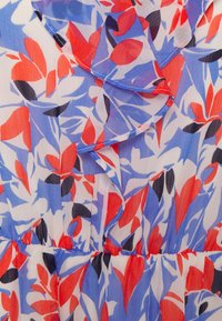 Blommig klänning med blå, röda och svarta bladmönster på lätt, genomskinlig tyg, med volangdetaljer vid halsen och midjan.