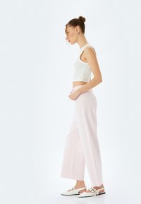 Pantalons en denim rose clair à jambes larges, dotés d'une taille haute et de poches arrière, associés à un crop top blanc et des chaussures plates blanches.