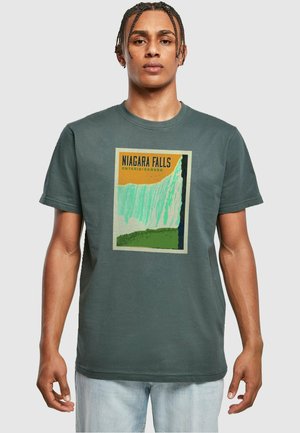 T-shirt en coton vert foncé avec un imprimé graphique des chutes du Niagara, agrémenté de touches de jaune et de vert. Col rond ; manches courtes.