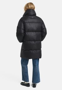 Zwarte pufferjack met een hoge kraag, voorzien van een geb quilt ontwerp en een verstelbare pasvorm. Draagt met flared jeans en donkere schoenen.