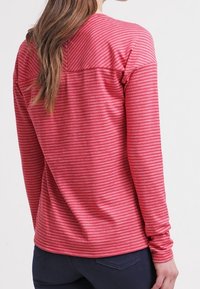 Camicia a maniche lunghe a righe rosse realizzata in tessuto morbido, con colletto rotondo e vestibilità comoda. Texture liscia, con dettagli sulle cuciture delle spalle.