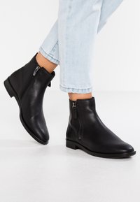 Botas de cuero negras hasta el tobillo con un diseño elegante y cremalleras laterales. Suelas opacas y planas, punteras redondeadas y un estilo minimalista.