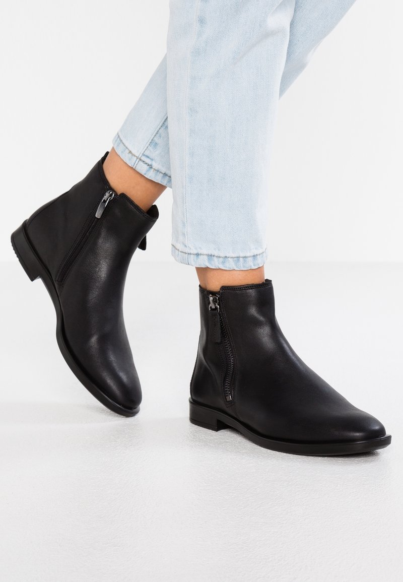Botas de cuero negras hasta el tobillo con un diseño elegante y cremalleras laterales. Suelas opacas y planas, punteras redondeadas y un estilo minimalista.