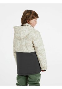 Hellfarbener Jacke mit Graffiti-Muster oben und dunklem Unterteil, ausgestattet mit einer Kapuze und elastischen Bündchen. Getragen mit grünen Hosen.