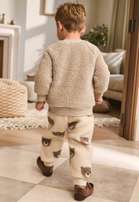 Beige fuzzy sweatshirt with a rounded neckline, paired with cream fleece pants featuring owl patterns. Brown slip-on shoes.