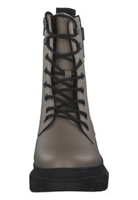 Botín beige hasta el tobillo con cordones negros, parte superior de cuero suave, puntera reforzada y suela de goma texturizada. Cuenta con una cremallera lateral para un acceso fácil.
