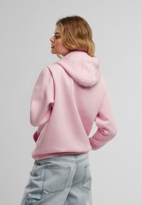 Hoodie rose clair en tissu doux, avec une capuche à cordon et des poignets côtelés, associé à un pantalon en denim bleu clair avec des poches.