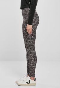 Leggings neri con stampa astratta bianca, design a vita alta, tessuto elastico, abbinati a sneakers bianche con dettagli verdi.