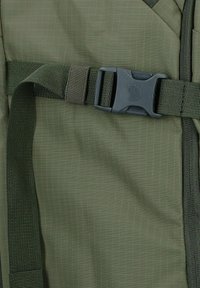 Mochila de tela verde con un patrón de cuadritos; cuenta con una correa ajustable de color verde oscuro y un broche de plástico gris para el cierre.