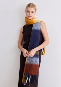 Écharpe en laine présentant un motif dégradé de nuances orange, marine, bleu clair et marron ; finie avec des franges aux extrémités.