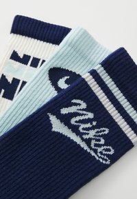 Trei perechi de șosete cu textură ribbed; culorile includ albastru marin, albastru deschis și alb cu accente sau modele și logo-uri.