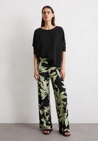 Black oversized sweater with long sleeves paired with wide-leg trousers featuring a green floral pattern on a black background. Black sandals.