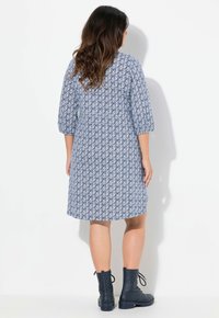 Blau gemustertes Kleid mit Dreiviertelärmeln, knielang, mit floralem Design. Kombiniert mit marineblauen Stiefeletten.