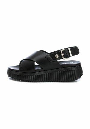 Sandalias de plataforma negras con un diseño de tiras cruzadas, hechas de cuero suave. Suela texturizada y correa ajustable en el tobillo con hebilla de metal.