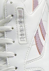 Gros plan d'une basket blanche Reebok montrant les lacets, le logo Reebok avec l'Union Jack, et un motif cousu violet et orange sur le côté.