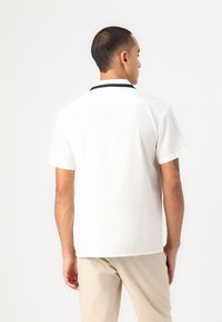 Short-sleeve white shirt with a black collar. Smooth fabric, relaxed fit, minimal design, visible stitching, and no patterns.
