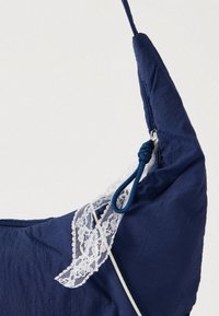 Meresinine kangas tekstuurse viimistlusega, millel on valge pitsaktsent ja sinine nöörihoidja, kujundatud moodsas kolmnurkses vormis.