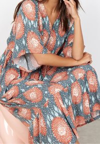 Blumenmusterkleid mit blauer Grundfarbe und orangefarbenen sowie weißen Akzenten, fließenden Ärmeln und lockerer Passform. Strukturierter Stoff.