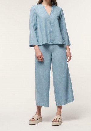 Haut en denim bleu clair avec un décolleté en V et des manches larges, associé à un pantalon en denim à jambe large, complété par des sandales à plateforme neutres.