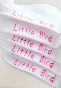 Calcetines de algodón blancos con el texto repetido en rosa "Pajarito". Presentan una textura suave y una forma estándar de calcetín.