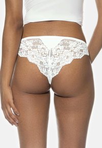Witte kanten string met bloemenpatronen, voorzien van zigzagranden en een gladde, ondoorzichtige voorkant. De stof heeft een delicate, ingewikkelde textuur.