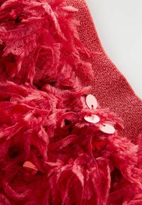Roter, strukturierteter Stoff mit fluffigen Fasern, akzentuiert durch glänzende, runde Pailletten, die ein schichtweise gestaltetes Design hervorheben.