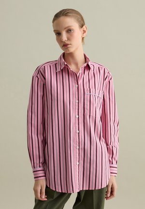 Roze gestreepte button-up shirt met zwarte lijnen, borstzak en knoopmanchetten. Gemaakt van soepel materiaal. Het shirt heeft een losse pasvorm en een klassieke kraag.