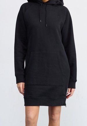 Robe à capuche noire à manches longues avec poche kangourou devant, capuche à cordon, poignets et ourlet côtelés portée par une personne debout.