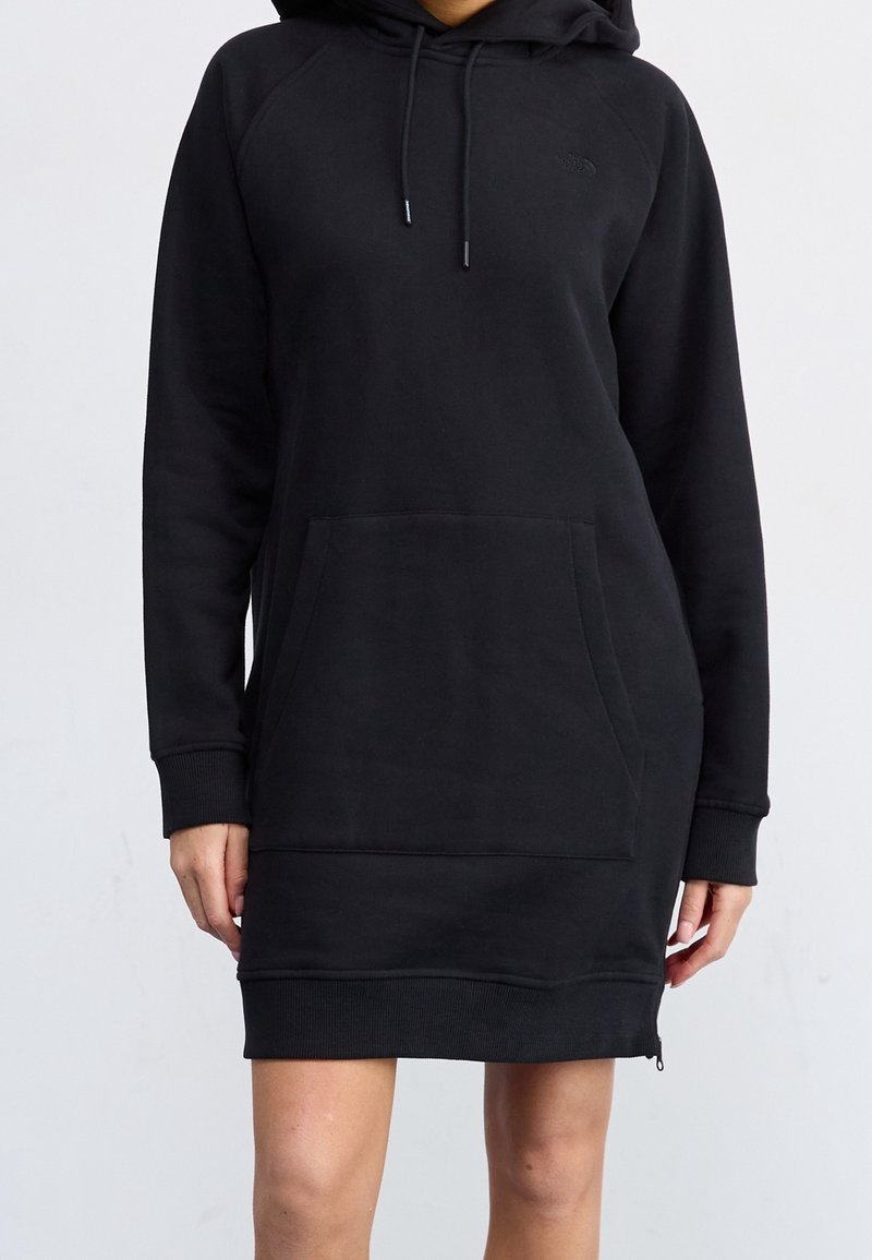 Robe à capuche noire à manches longues avec poche kangourou devant, capuche à cordon, poignets et ourlet côtelés portée par une personne debout.