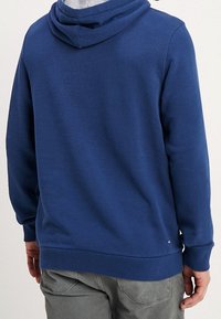 Sudadera con capucha de algodón azul marino con cordón ajustable en la capucha, puños y dobladillo acanalados, y un pequeño detalle de logo cerca del borde inferior.