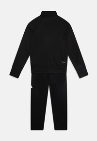 Survêtement de sport noir, comprenant une veste zippée avec un col haut et des manches longues, associé à un pantalon fuselé assorti. Texture lisse.