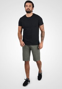 Tricou negru cu model de buline albe, asortat cu pantaloni scurți verzi. Purtați cu adidași negri, are mâneci scurte și un decolteu rotund.