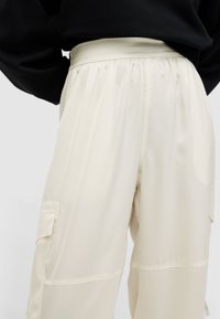 Crème-kleurige cargo broek van soepel materiaal, met een elastische tailleband en zijzakken, met een relaxte pasvorm en een lichte glans.