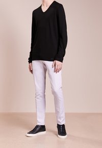 Maglione nero a maniche lunghe con scollo a V, abbinato a pantaloni bianchi slim-fit e sneaker in pelle nera. Il tessuto sembra morbido e textured.