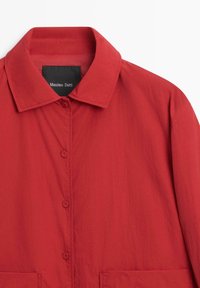 Red, lightweight jacket with a collar, front buttons, and two front pockets. Features a smooth texture and a minimalist design.