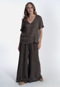 Top in lino marrone con scollatura a V e maniche corte arrotolate, abbinato a pantaloni ampi coordinati e sandali leggeri intrecciati.