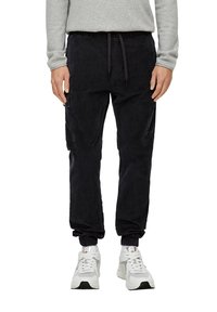 Czarne dżinsowe joggery z elastycznym paskiem w talii i ściągaczami, z bocznymi kieszeniami i luźnym krojem. Połączone z białymi sportowymi trampkami.