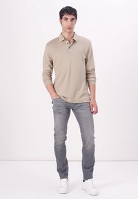 Beige long-sleeve polo shirt with a collar, paired with light gray jeans and white sneakers. Simple design, smooth texture, and straight fit.