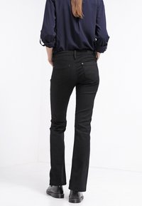 Jeans negros de cintura acampanada con una textura suave, que presentan una cintura ajustada y dos bolsillos traseros. Combinados con una camisa de manga larga color marino.