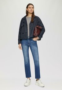 Veste cropped marine à boutons croisés sur une chemise grise, assortie à un jean droit bleu et des baskets blanches épaisses.