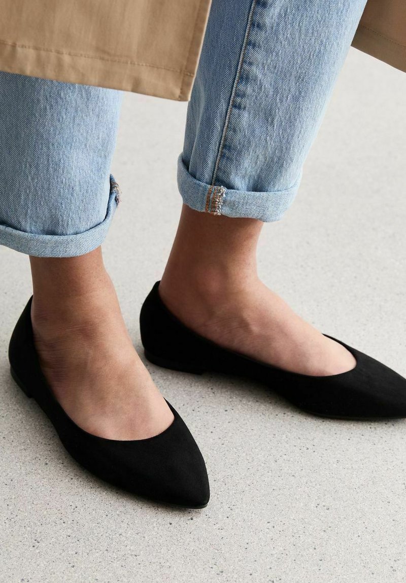 Svarta mocka baletttofflor med spetsig tå, bärs med rullade ljusblå denimjeans. Platt sula, minimal design, ingen synlig hårdvara.