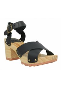Sandale en cuir noir avec des brides croisées, talon en bloc de bois, clous en laiton et bride de cheville ajustable ; semelle en bois avec une finition texturée.