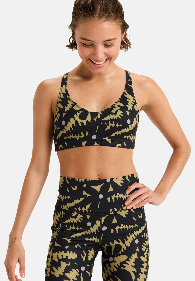 Un reggiseno sportivo nero e leggings con un motivo foglioso verde e bianco. Realizzati in tessuto elasticizzato con una texture liscia e un design aderente.